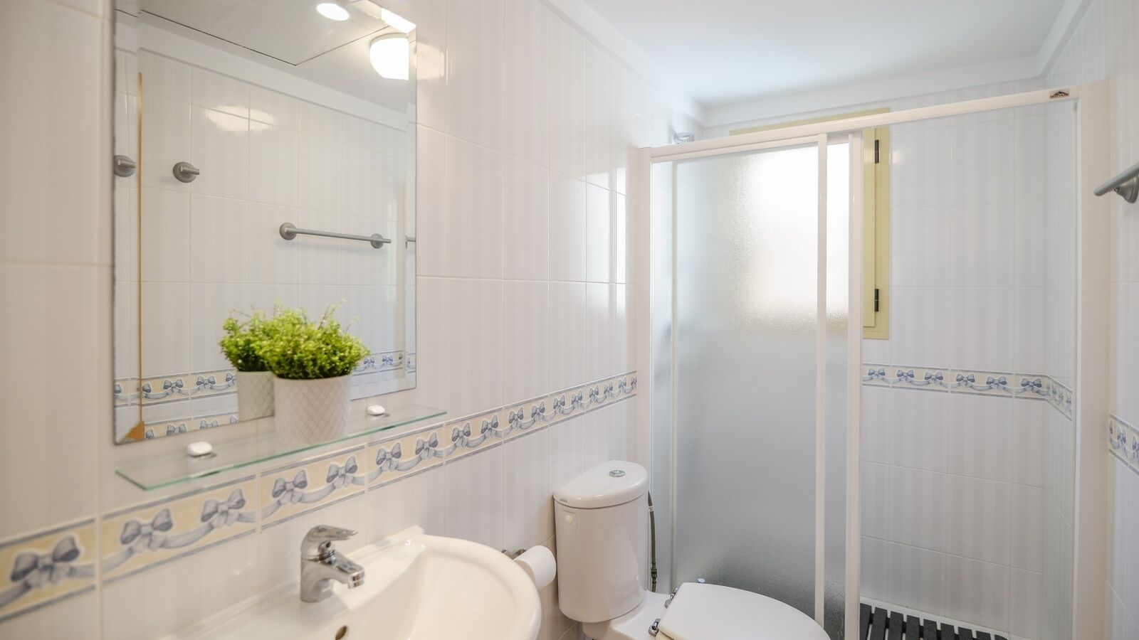 A bathroom with a glass shower enclosure, a sink with a mirror, and a toilet.