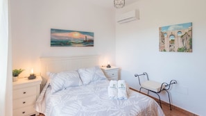 Un dormitorio con cama, mesitas de noche, sillón y obras de arte en las paredes.