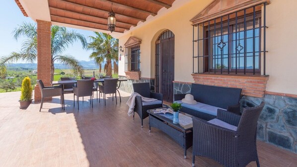 A covered patio with outdoor furniture, a stone wall, and a view of the landscape. - La Era de Coín by Ruralidays (Málaga)