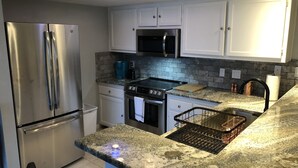 Una cocina moderna con electrodomésticos de acero inoxidable, encimeras de granito y armarios blancos.