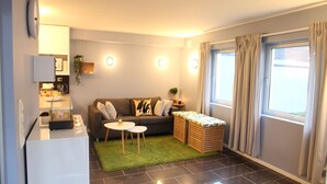 Um espaço compacto com sofá, mesa pequena para refeições, área de cozinha e janela com cortinas.