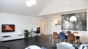 Uma sala de estar moderna com lareira, área de jantar e uma grande pintura de uma floresta.
