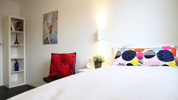 Habitación de hotel con una cama, una estantería, una silla roja, un reloj de pared y una planta en maceta.