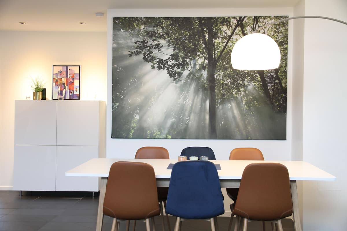 A modern dining area with a large forest-themed wall art, a white table, and brown chairs.