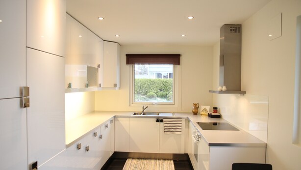 Uma cozinha moderna com armários brancos, piso de azulejos pretos, janela com vista e coifa de aço inoxidável.