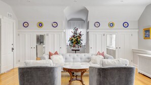 Ein geräumiges Wohnzimmer mit einem weißen modularen Sofa, zwei grauen Sesseln, einem Marmor-Couchtisch und einer floralen Dekoration.