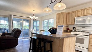 A spacious kitchen with wooden cabinets, a large island with bar stools, a white stove, and a microwave. - Rf12 Flathead River Haven (Columbia Falls)