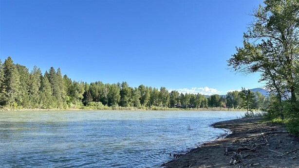 A riverbank with a clear view of a forest and distant mountains. - Rf12 Flathead River Haven (Columbia Falls)