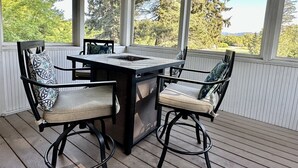 A covered patio with a table and chairs, large windows, and a view of trees and hills. - Rf12 Flathead River Haven (Columbia Falls)