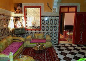 A traditional Moroccan room with patterned tiles, a checkered floor, and a sofa with a pink throw. - Riad Konouz (Marrakech)