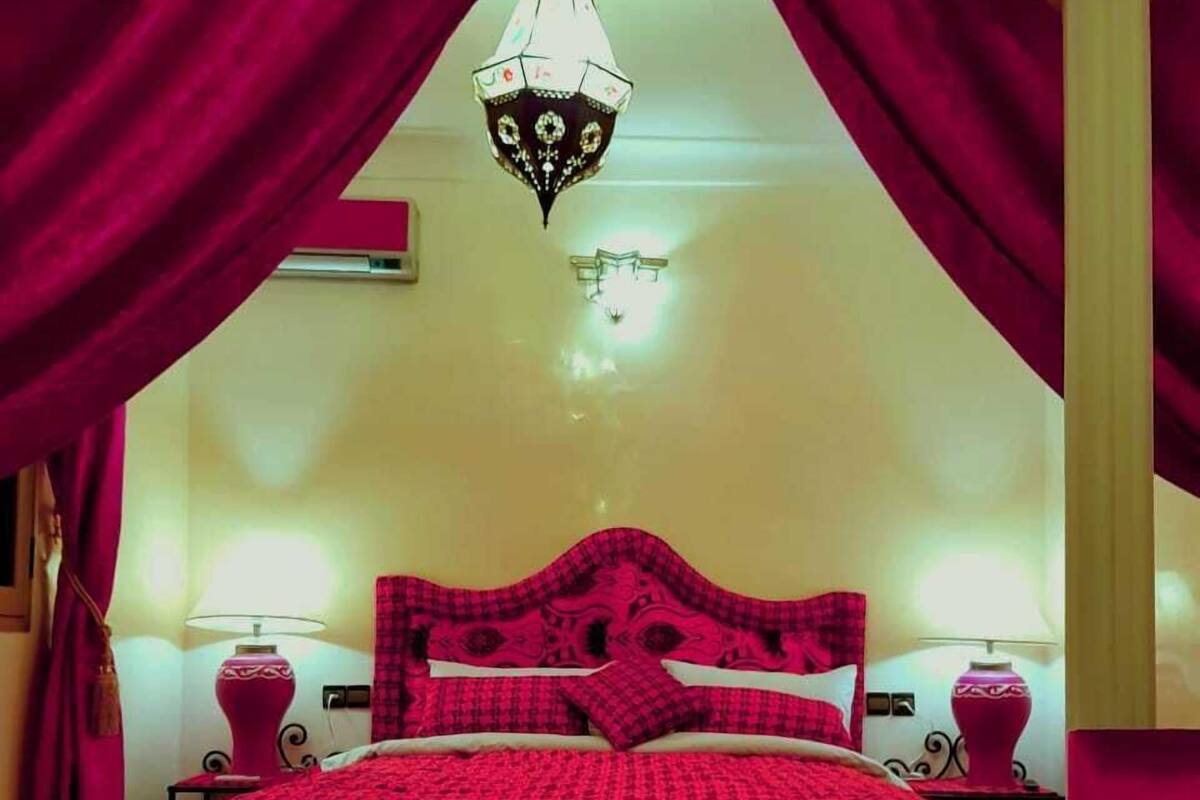 Une chambre à coucher avec un grand lit, deux tables de chevet, un lustre et un tapis à motifs.