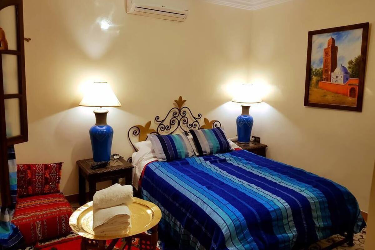Une chambre d’hôtel avec un lit, deux lampes de chevet, un tableau, une chaise rouge et un plateau avec une serviette.