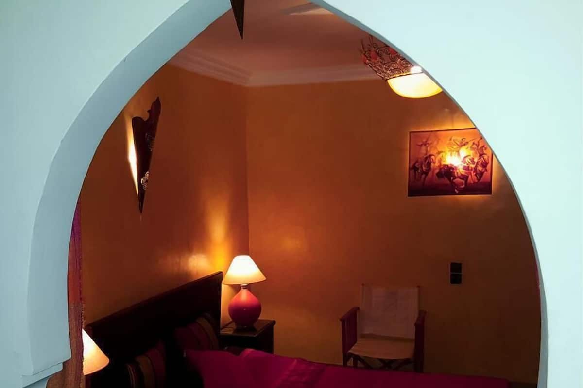 Une chambre confortable avec un grand lit, une lampe de chevet, un fauteuil et un tableau accroché au mur.