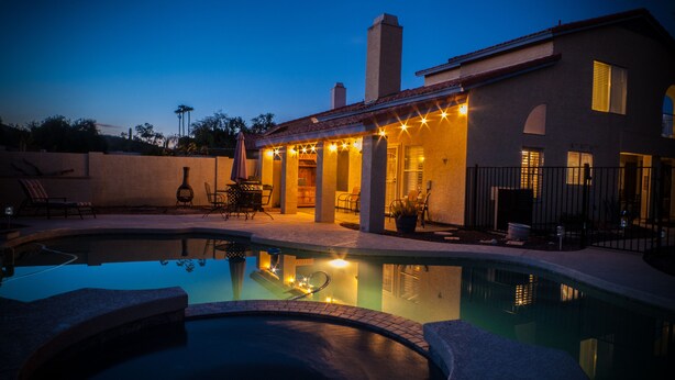Area piscina con idromassaggio, posti a sedere all'aperto e patio coperto con luci decorative.