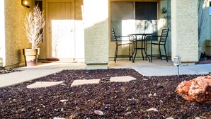 Una veranda coperta con tavolo e sedie, una pianta in vaso e un sentiero in pietra che porta a una porta.