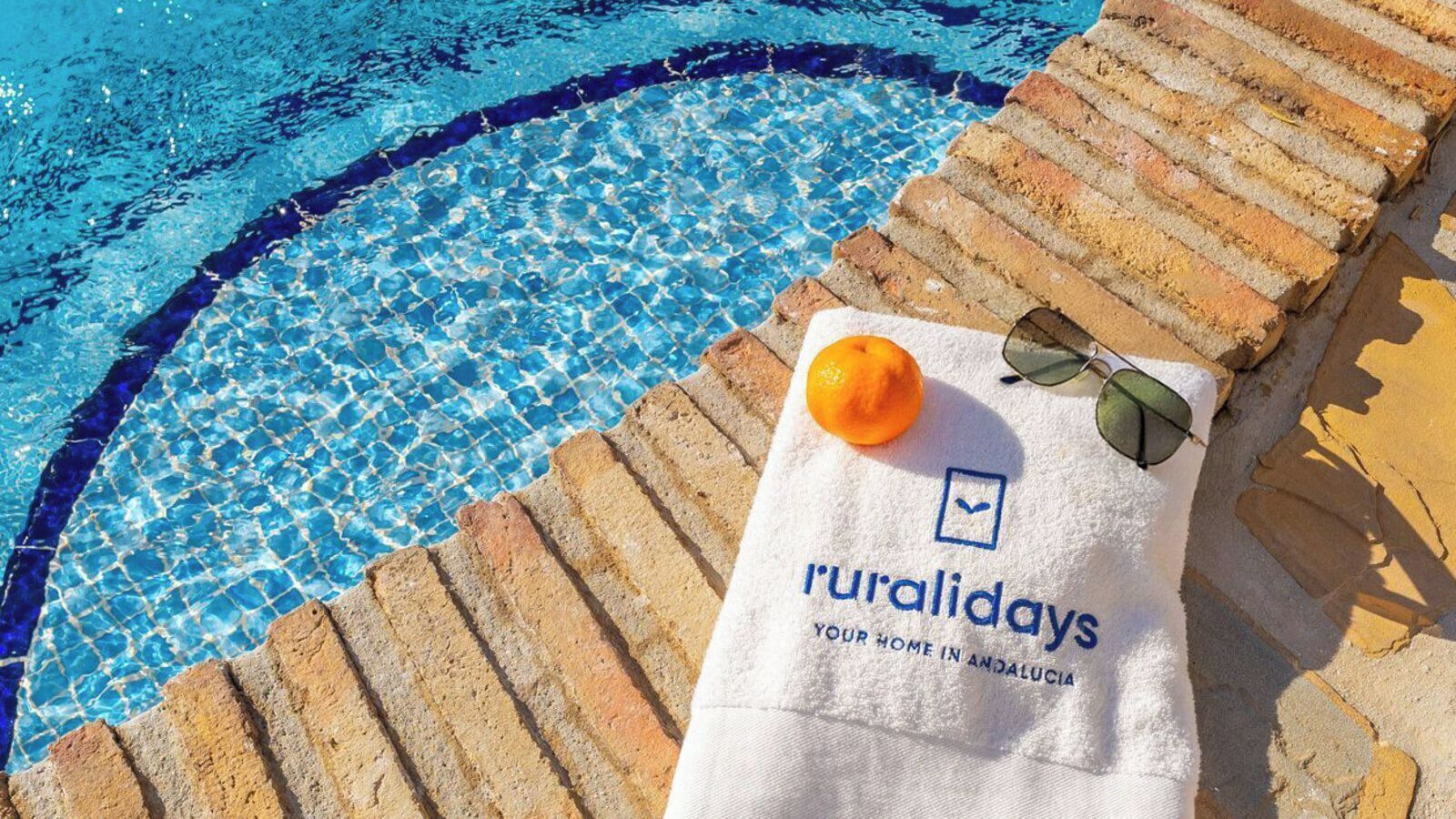Un espace aménagé au bord de la piscine avec une serviette, des lunettes de soleil et une orange.