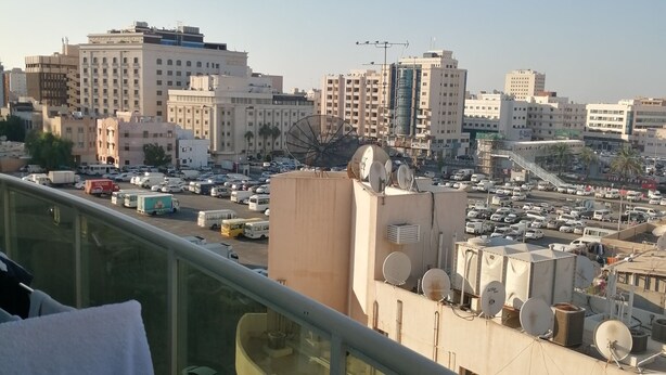 A balcony with a view of a cityscape, including buildings and parked cars.