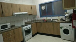 A kitchen with wooden cabinets, a microwave, an oven, a sink, and a washing machine.