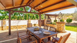 An outdoor patio with a wooden table set for dining, stone walls, and a stone pillar. - La Pedrosa Setenil de las Bodegas by Ruralidays (Cádiz)