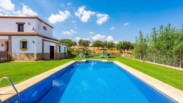A rectangular swimming pool with a clear blue water surface, surrounded by a well-maintained lawn and a white building with a tiled roof. - La Pedrosa Setenil de las Bodegas by Ruralidays (Cádiz)