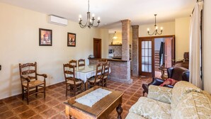 A living room with a glass-top dining table, wooden chairs, a patterned sofa, and a fireplace. - La Pedrosa Setenil de las Bodegas by Ruralidays (Cádiz)