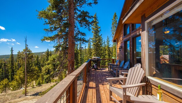 Ett trädäck med Adirondack-stolar, med utsikt över ett skogsområde.