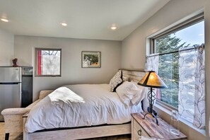 A bedroom with a bed, a nightstand, a lamp, a window with curtains, and a refrigerator. - Cozy Mountain Studio By Main Street & Hot Springs! (Buena Vista)