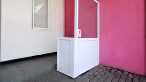 Eine weiße Tür mit Glasfenster, neben einer roten Wand und einem Fenster mit Rollläden.