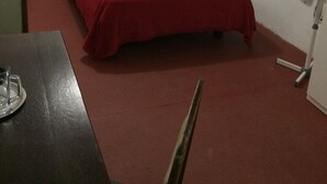 Una habitación con cama, una mesa y una silla. Hay dos espejos en las paredes.