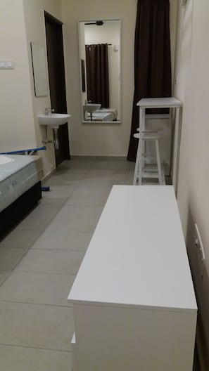 A small, clean room with a bed, a white table, a white shelf, a white sink, and a mirror. - GLG KLIA Transit House (Sepang)