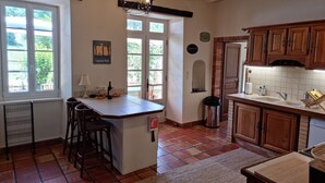 Una cocina con isla central, armarios de madera, piso de baldosas y ventana con vistas a la vegetación.