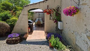 Un patio con mesa y sillas, una parrilla y plantas en macetas.