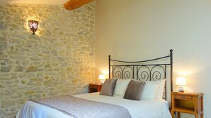 Un dormitorio con pared de piedra, estructura de cama metálica y dos mesitas de noche con lámparas.