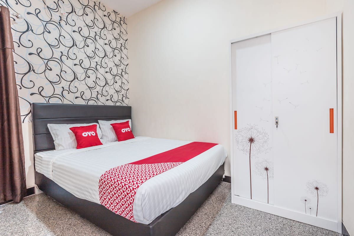 A neatly made bed with a white and red patterned bedspread, a black headboard, and two red pillows with the word "OYO" on them.