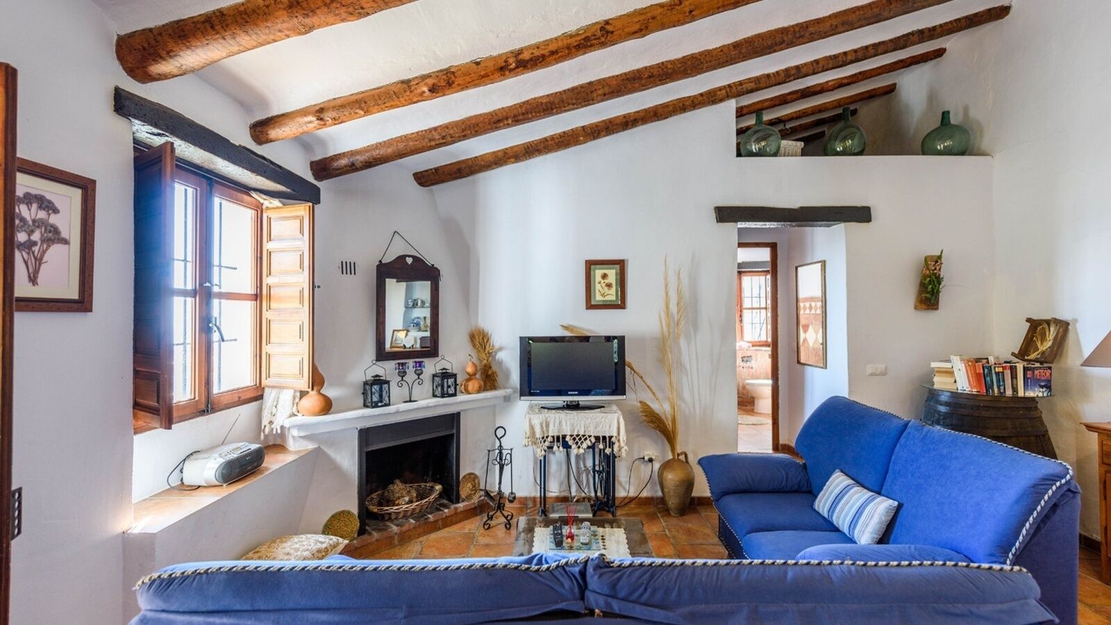 A cozy living room with a fireplace, a blue sofa, and wooden beams on the ceiling.