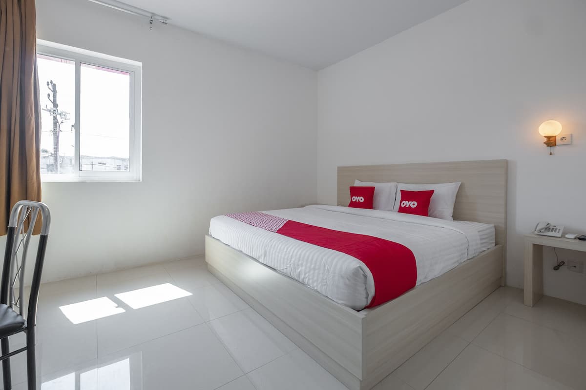 Une chambre d’hôtel avec un lit, une chaise, une table de chevet et une fenêtre.