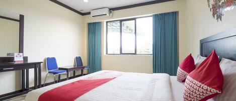 Habitación de hotel con cama, dos sillas, un escritorio y una ventana con cortinas.