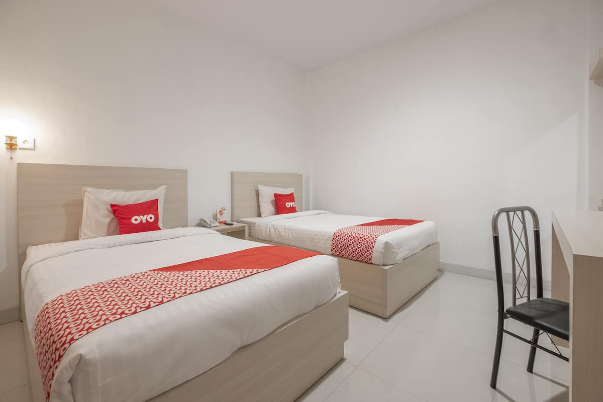 Une chambre d’hôtel avec deux lits, chacun recouvert d’une courtepointe rouge et blanche, dotée d’une tête de lit en bois et d’une table de chevet avec un téléphone.