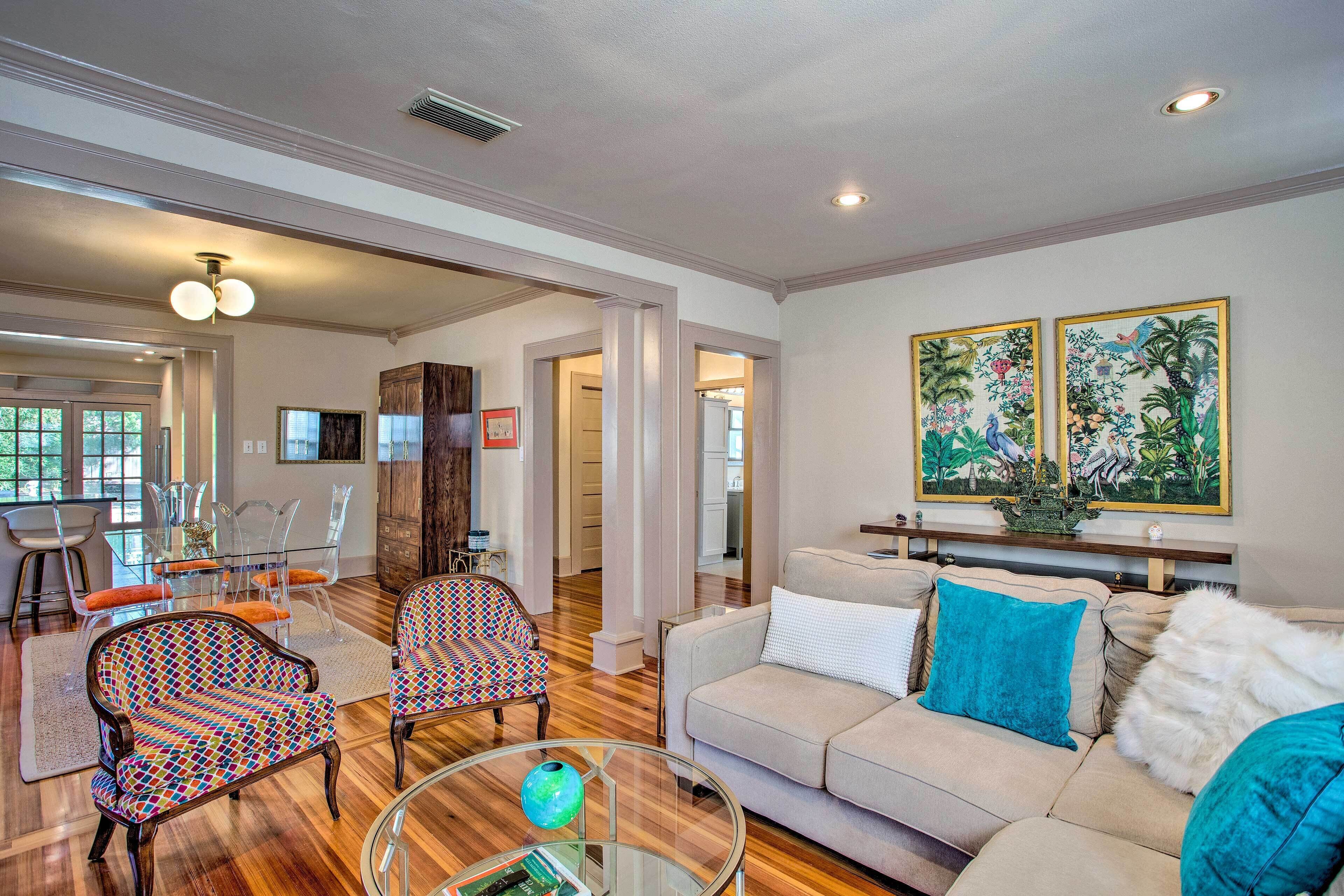 A spacious living room with a beige sofa, patterned chairs, a glass coffee table, and a dining area with clear chairs and a glass table.
