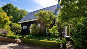 Une maison noire avec un toit gris, entourée de jardins et d’arbres bien entretenus.