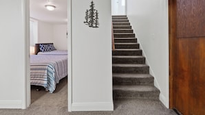 Ein Flur mit Teppichstufen, einer Holztür und einem Schlafzimmer mit Bett und Fenster.