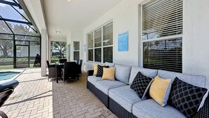 A covered patio area with a pool, outdoor seating, and a sign indicating pool rules. - This amazing 6 Bedroom property with a lake view is spacious and newly furnished (Kissimmee)