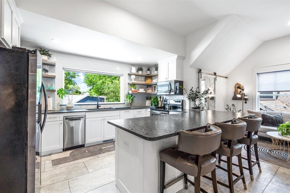 Een moderne keuken met witte kasten, een centraal eiland met barstoelen, en een groot raam met uitzicht op groen.