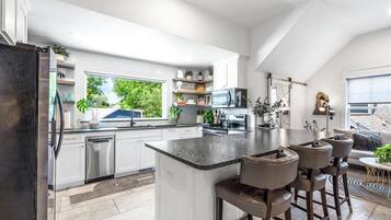 Een moderne keuken met witte kasten, een centraal eiland met barstoelen, en een groot raam met uitzicht op groen.