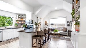 Una cucina moderna con isola centrale, sgabelli da bar e zona pranzo con divano e tavolino.