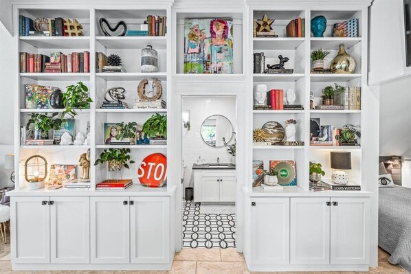 A well-organized room with white cabinetry, a tiled floor, and a variety of decorative items and books.