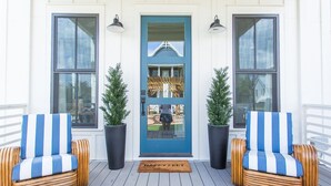 Une véranda avec deux fauteuils en osier, une porte bleue et des plantes en pot.