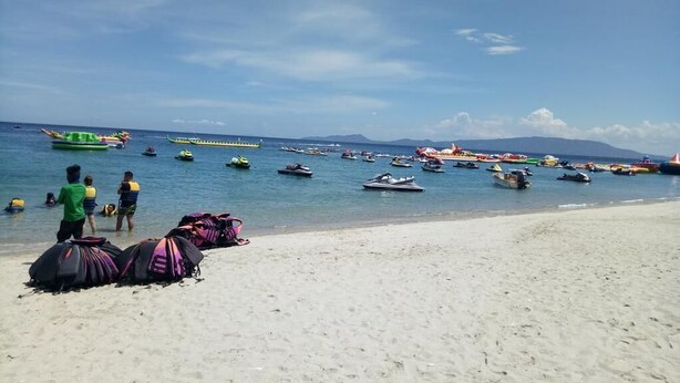 Una playa con numerosos barcos y gente en el agua.