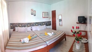 Una cama doble con ropa de cama a rayas, una mesita de noche con un jarrón de rosas rojas y un televisor sobre una repisa.