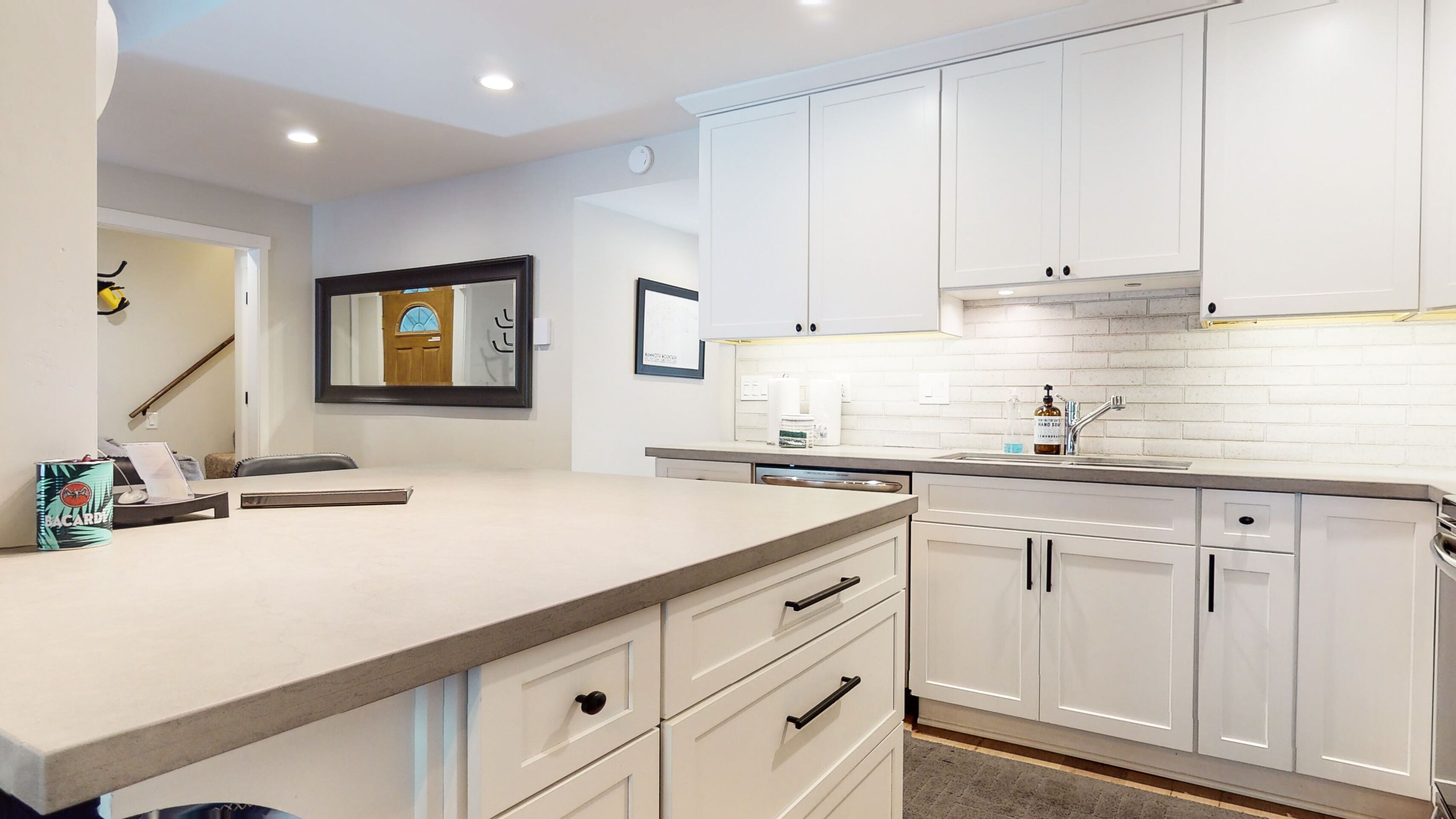 Una cocina moderna con armarios blancos, una isla grande con fregadero y un salpicadero de azulejos.